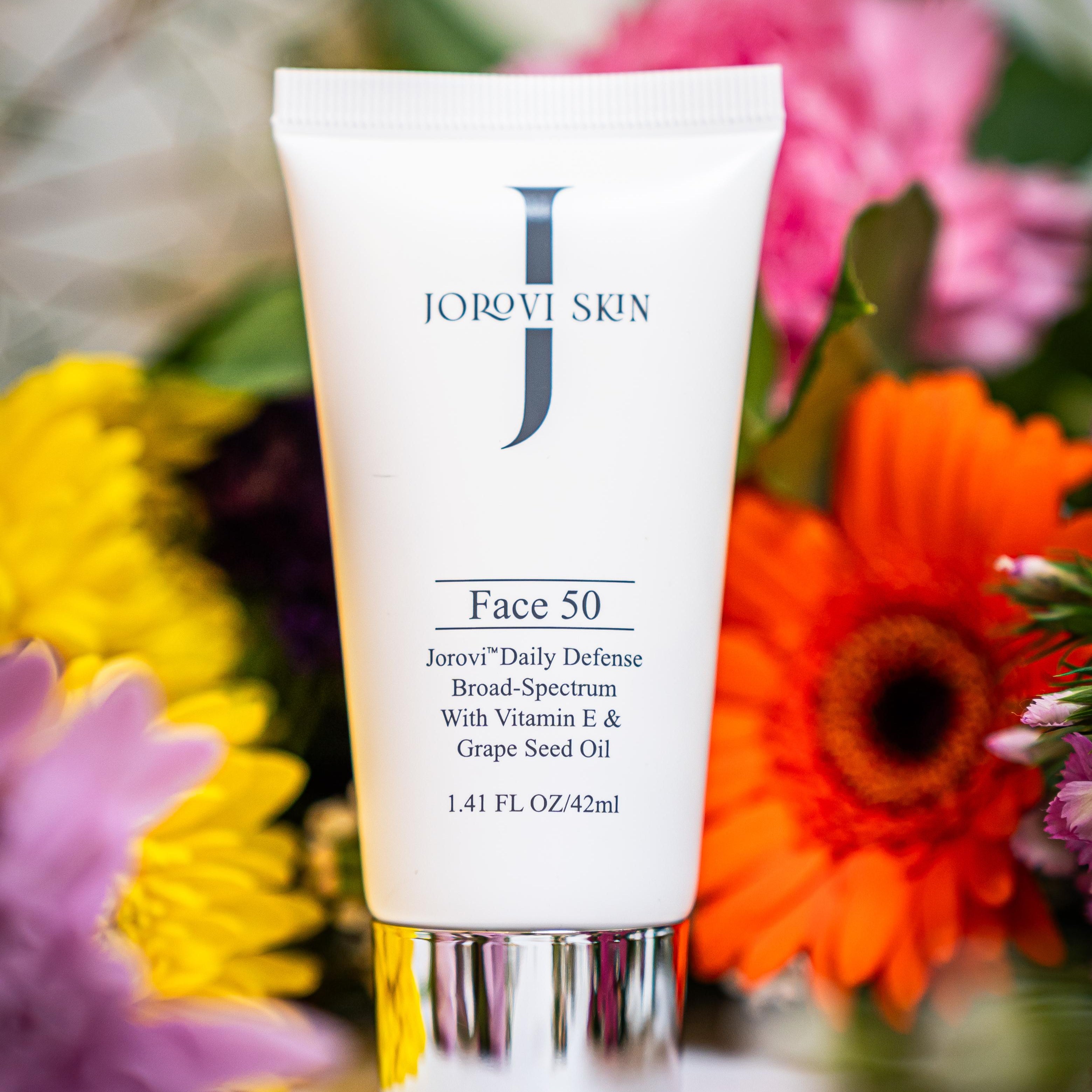 Tube of Jorovi Skin Face 50 sunscreen with flowers in the background jorovi face 50 broad spectrum
